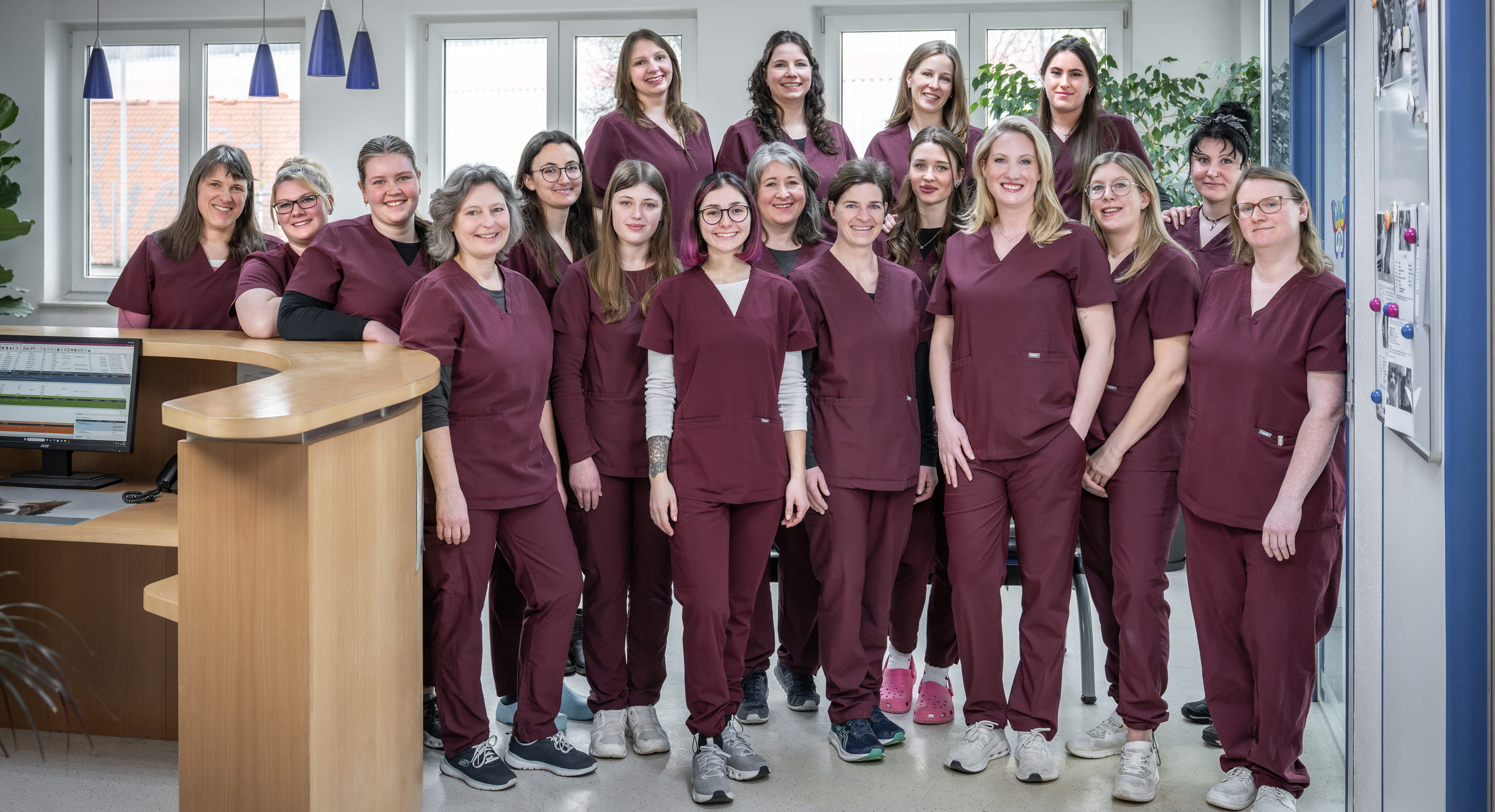 Praxisteam in bordeauxfarbenen Arbeitskitteln am Empfang